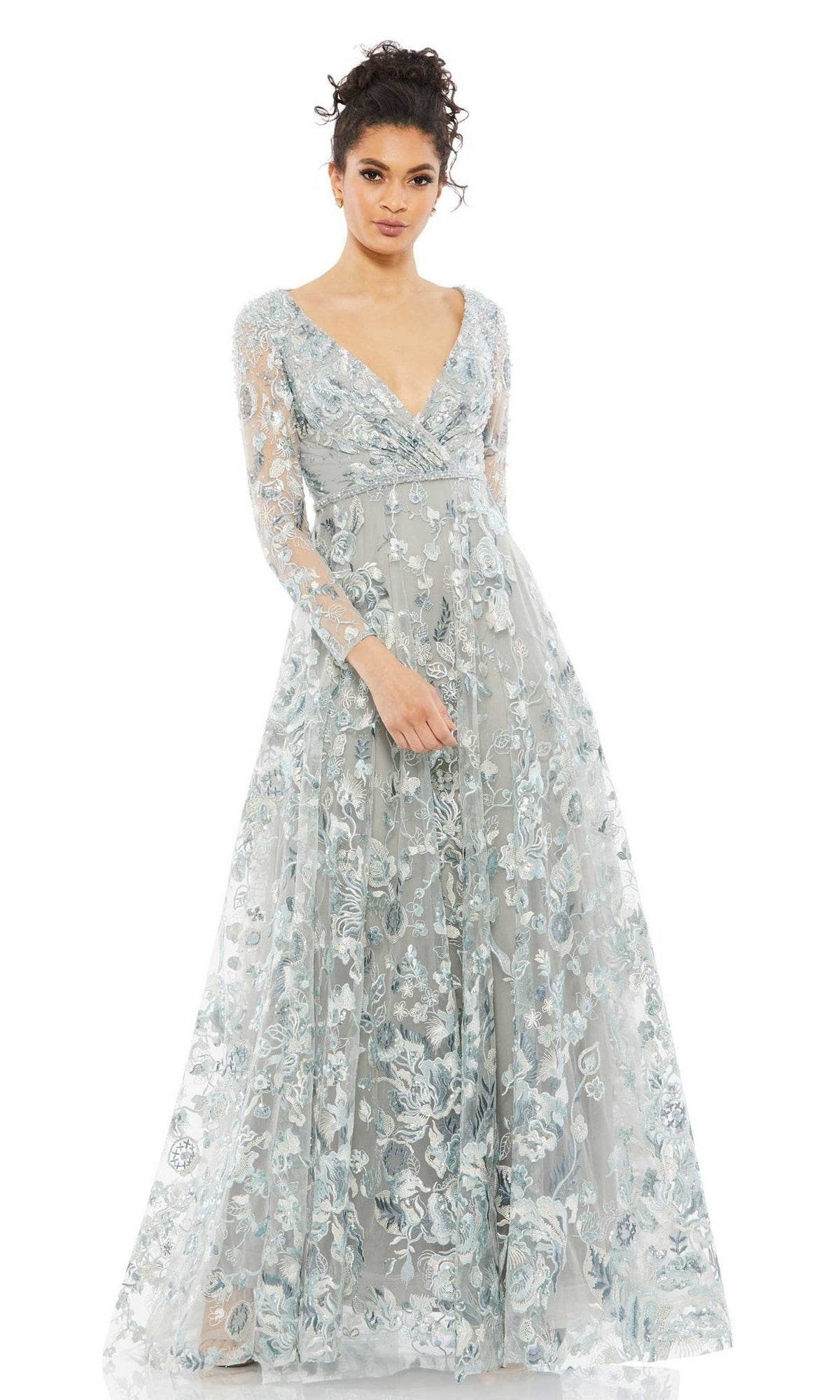 A woman wears the Mac Duggal 67869 Long Sleeve Lace Formal Dress, featuring a light blue-grey color, floral embroidery, sheer long sleeves, and a deep V-neck—an ideal mother of the bride gown.